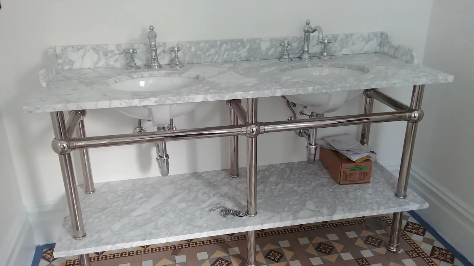 Finished double vanity sink installation with polished chrome exposed plumbing and marble countertop