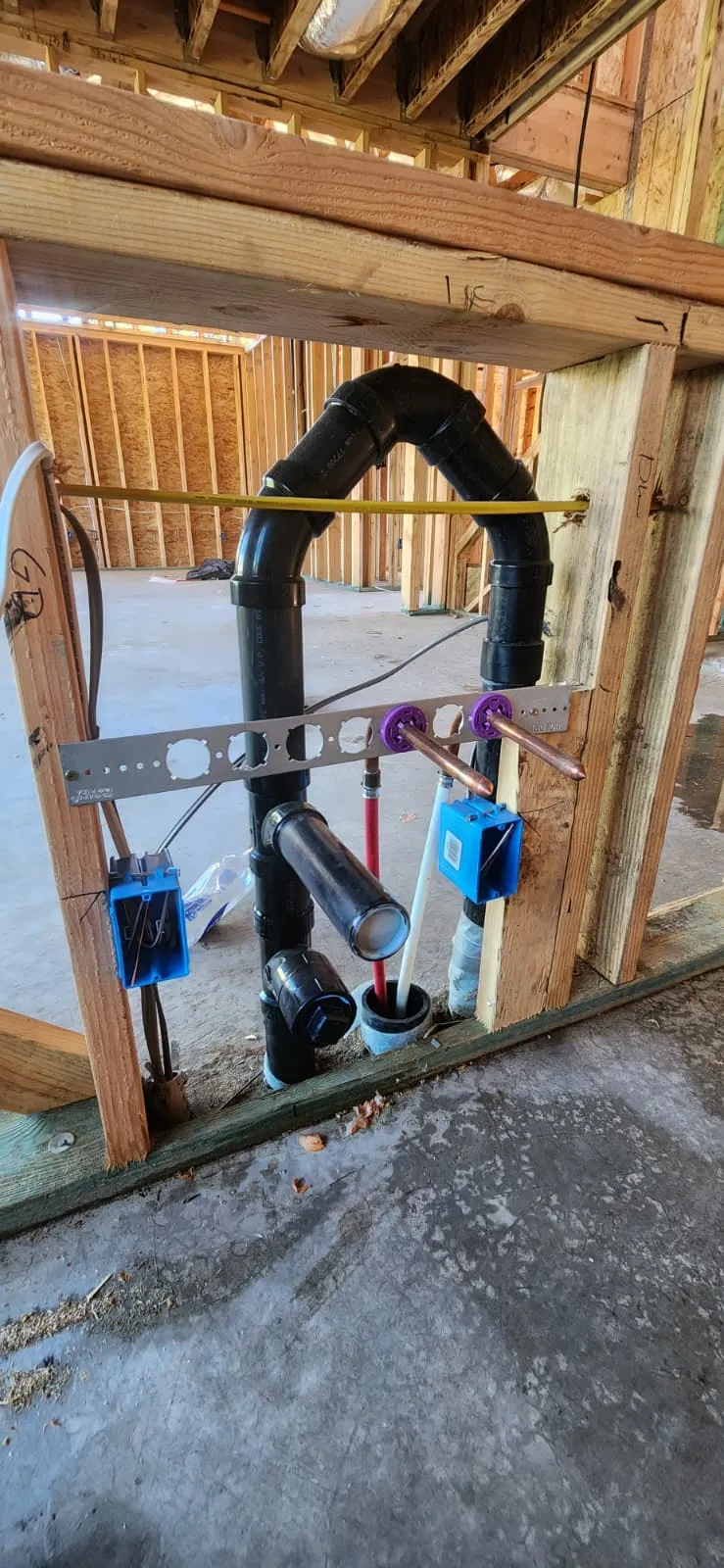 Rough-in plumbing installation — exposed wall studs with copper supply pipes, PVC drain lines, pre-drywall stage, bright construction interior